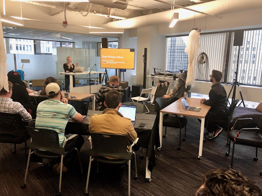 A woman in front of a TV speaks to a crowd, explaining how to play a data privacy themed version of the card game, taboo.